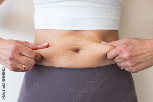 Bild auf Leinwand Woman in activewear pinching her abdomen to show body fat