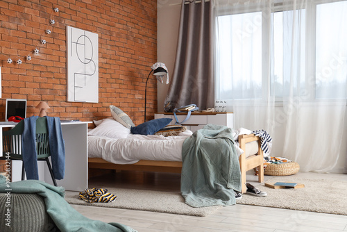 Interior of messy teenager's room with bed and workplace