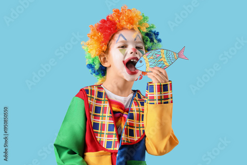 Funny little boy in clown disguise with paper fish on blue background. April ...