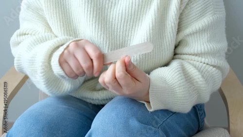 A woman sitting on a chair and doing manicure with a nail file.