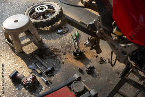 Motorcycle repair in messy garage workshop, with detached wheel and scattered tools on dirty floor. gritty scene of vehicle maintenance and hands on work
