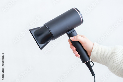 Fotografie Hand holding black hair dryer against gray background close-up.