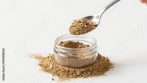 A Spoonful of Ground Spice Being Poured Into a Glass Container on a White Background