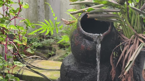 A serene view of a stone water jar fountain nestled among vibrant green ferns and tropical plants.