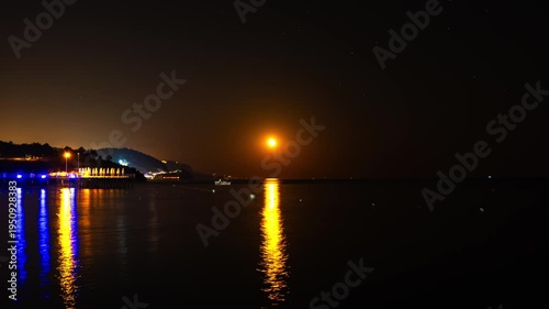 Timelapse Moonlight Over Sea Waves Full Moon Glow ocean waves on sandy beach at night wooden pier. The moon illuminates water surface. Concept of beach vacation slowing down on seacoast. Travel