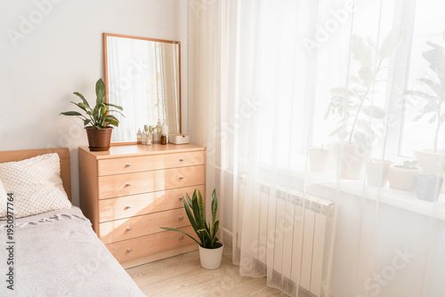Wooden dresser in a modern bedroom interior, displaying a mirror, decorative plant, and various beauty bottles on top