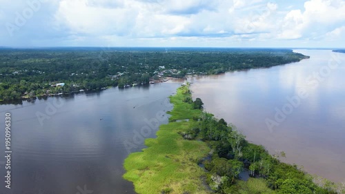 A serene aerial perspective of the Amazon River at Leticia, with vibrant green banks and cloudy skies visible.