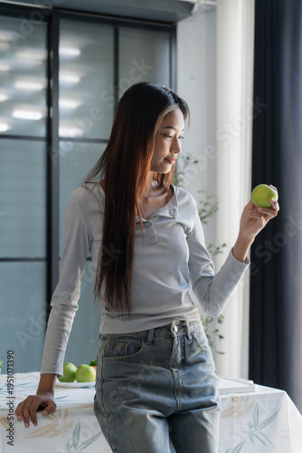 Asian woman standing and holding green apple in front of table