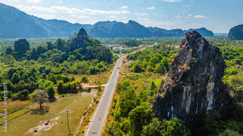 Fotografi A breathtaking landscape of towering rocky mountains rising dramatically above vibrant green plains, showcasing the untouched natural beauty of rural Laos