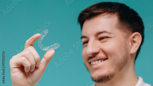 Smiling young man holding a clear aligner for dental orthodontic treatment and cosmetic teeth care