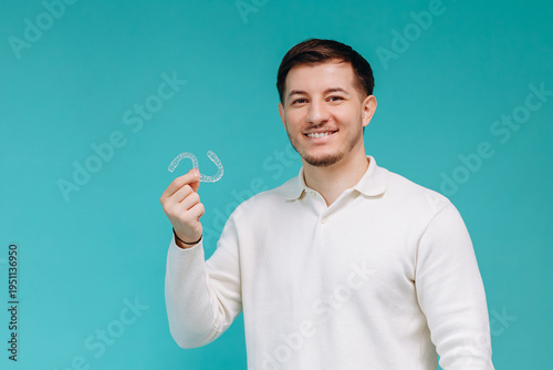 Smiling man holding clear dental aligner for orthodontic teeth straightening and dental care