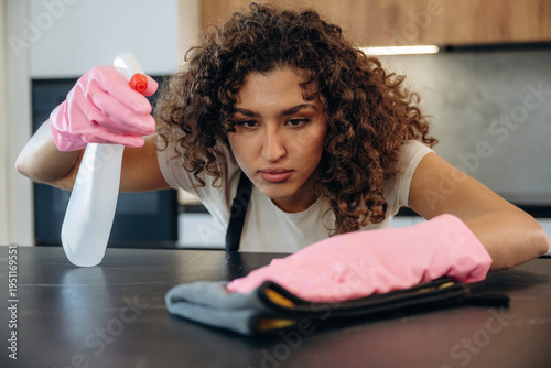 Cleaning the surface. White woman on the the kitchen countertop with spray and cloth wearing pink gloves