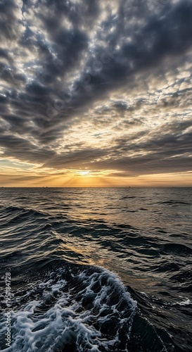 Sunset over ocean with cloudy sky.