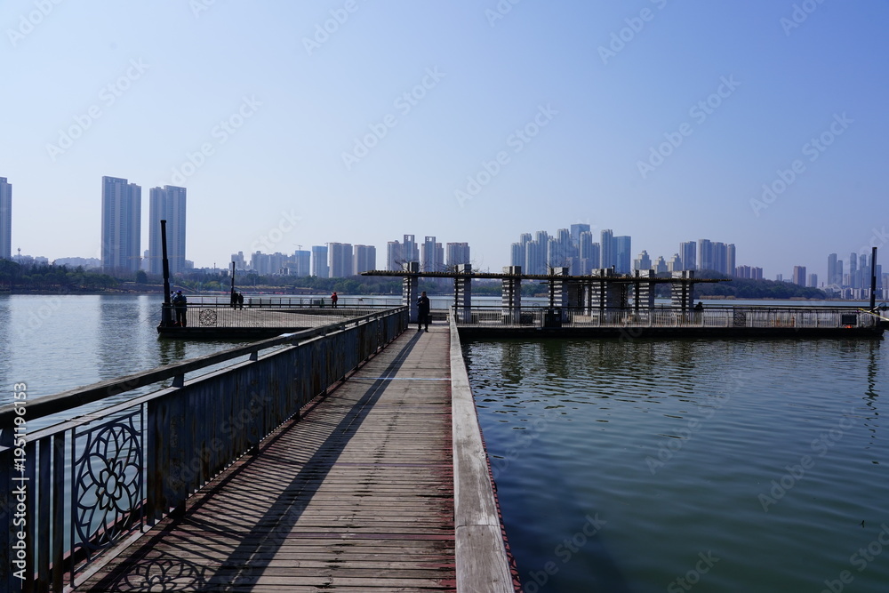Fototapeta premium Harbor walkway with railing leading toward a city skyline over water