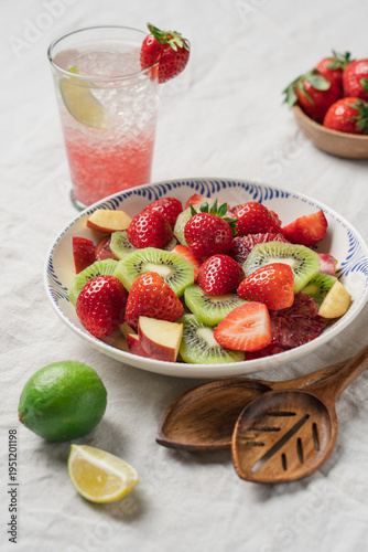 Summer brunch with fresh strawberry fruit salad and refreshing iced lemonade on table with linen tablecloth, healthy seasonal breakfast concept