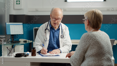 Fotografie Male doctor using recovery medication to give prescription paper to retired patient in medical office