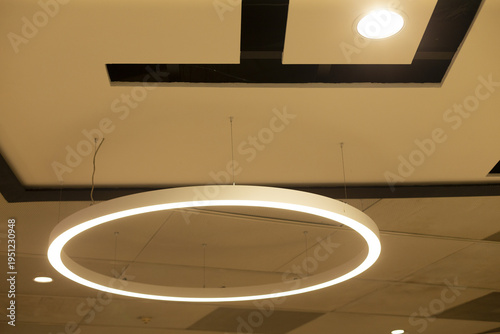 Bild auf Leinwand Suspended circular LED ring casting soft halo against geometric ceiling cutouts,