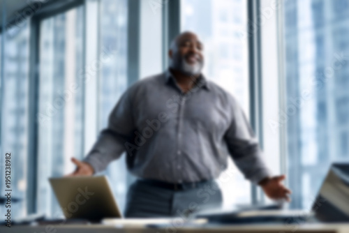 Blurred Confident businessman standing in modern office with laptop
