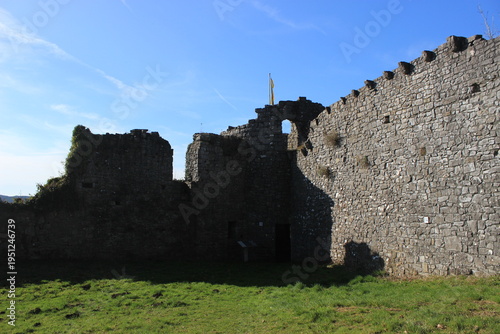Fotografie Ancient stone castle ruins stand against a clear blue sky with a yellow flag fly