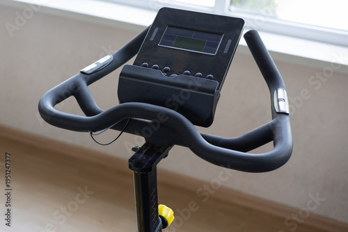 Close-up of a modern stationary exercise bike handlebars and digital console in a bright room.  Fitness equipment for home workout. 