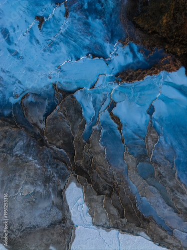 Aerial view of textured, icy formations cascade in shades of blue and gray, creating a stark contrast in the Grindavikurbaer landscape, Grindavikurbaer, Iceland.