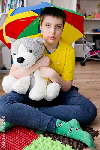 An autistic boy holds a colorful umbrella and a large plush toy. April is Autism Awareness Month.