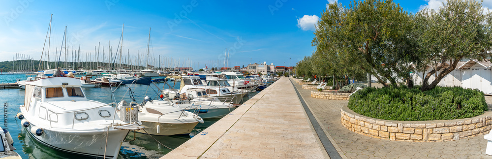 Fototapeta premium Pirovac, Croatia. Marina with small boats docked along a clean waterfront promenade. The scene conveys leisure boating, tourism, and Mediterranean lifestyle
