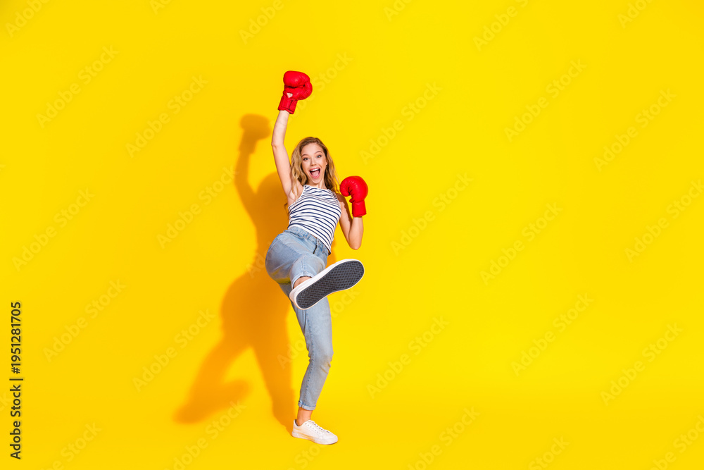 Fototapeta premium Joyful woman in casual clothing wearing red boxing gloves enthusiastically posing against a bright vibrant yellow background