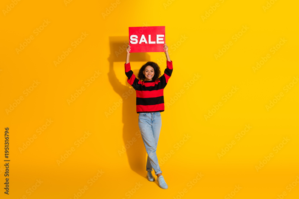Fototapeta premium Young woman model holds sale sign against bright yellow background promoting discount shopping and fashion