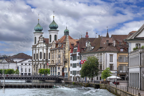 Jesuit Church and Reuss river with rushing water weir in Lucerne, Switzerland. Cloudy June sky in summer day