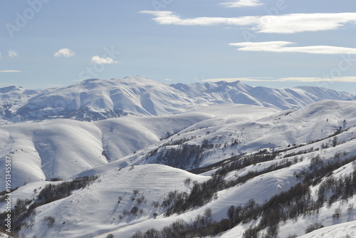 a vast mountain range under a pale blue sky with wispy white clouds the rolling hills