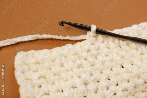 Fotografie Crochet fabric square with hook and yarn on brown background