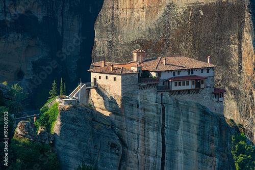 Unesco world heritage site roussanou monastery on a steep meteora rock formation amidst green trees, showcasing spiritual isolation and a unesco world heritage site. Meteora, greece