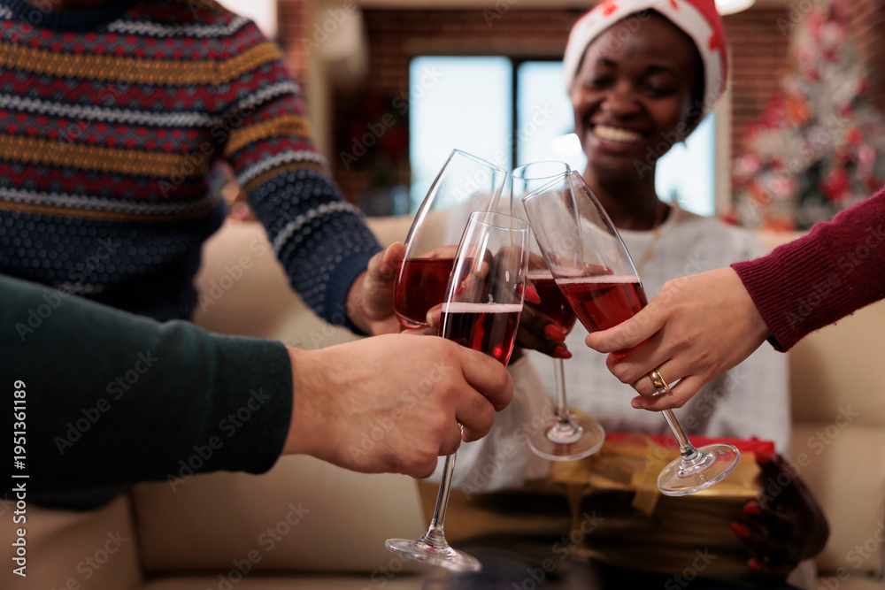 Obraz premium Group of people clinking glasses of wine on xmas eve, celebrating christmas office party with alcoholic beverage and festive toast. Toasting and saying cheers at holiday festivity.