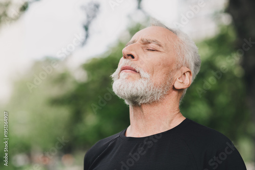 Serene elderly man with white beard enjoys outdoor park scene in calm morning light breathing deeply for a peaceful moment of wellness and fitness