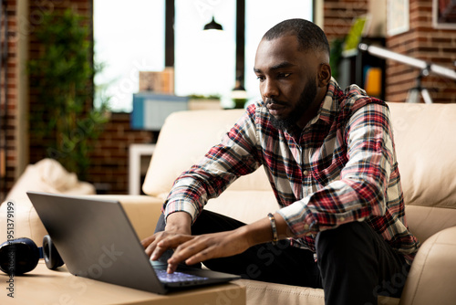 Εκτύπωση καμβά Serious male manager seated in cozy home office, typing on laptop and reviewing financial data