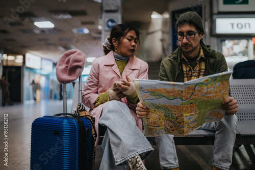 Foto Two tourists sit on a bench at a station studying a city map