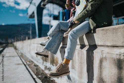 Photos Two tourists sit on the edge of a station platform holding a map and luggage