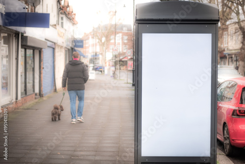 LONDON - Blank digital advertising kiosk on high street pavement with pedestrians