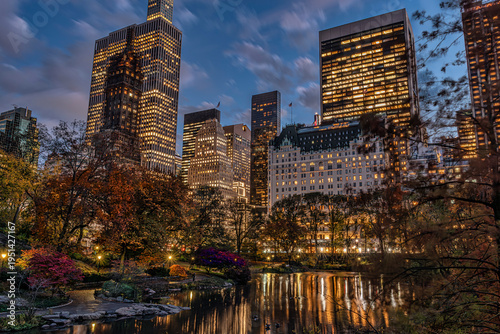 City skyline at dusk with reflections on a tranquil park pond and autumn foliage. Central Park Lake, New York City, USA