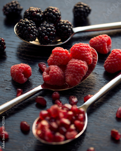 Close-up of spoons with raspberries, blackberries, and pomegranate seeds on a wooden surface.