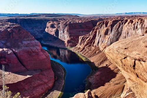 A winding river flows through a vast canyon under a clear blue sky with rugged orange cliffs. Horseshoe Bend, Colorado River, Arizona, USA