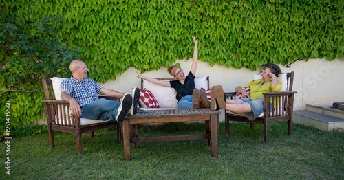 Group of middle aged friends relaxing with legs up and laughing together on outdoor garden patio on a sunny day