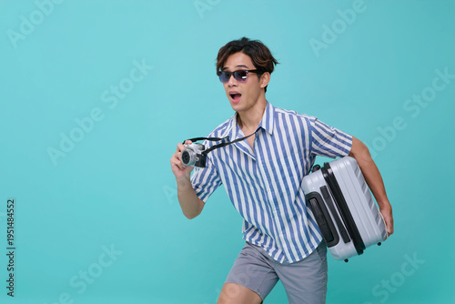Asian man holding suitcase and camera walking in studio expressing travel lifestyle vacation planning adventure journey tourism excitement and modern holiday concept