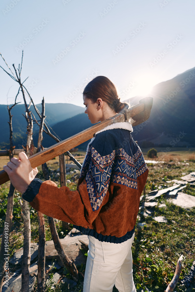 Fototapeta premium Woman with guitar outdoors in mountains at sunset, walking along trail wearing patterned sweater and light pants, backlit scene with natural landscape, peaceful travel and music.