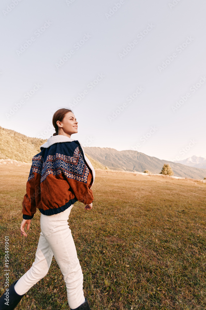 Fototapeta premium Woman walking in mountains meadow wearing patterned sweater and warm boots, enjoying autumn landscape and open field, outdoor lifestyle, travel and nature escape.