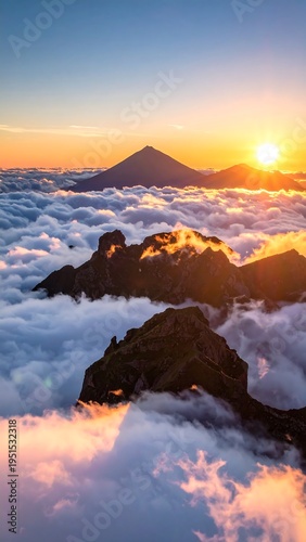 Majestic mountain peaks pierce through a sea of clouds under a vibrant, golden sunrise sky