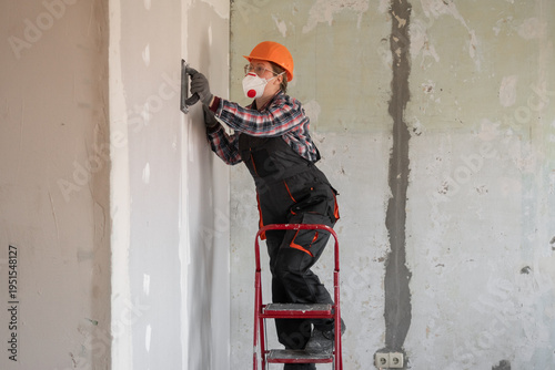 Фотография Woman builder or repairman with an emery tool sanding a plastered wall