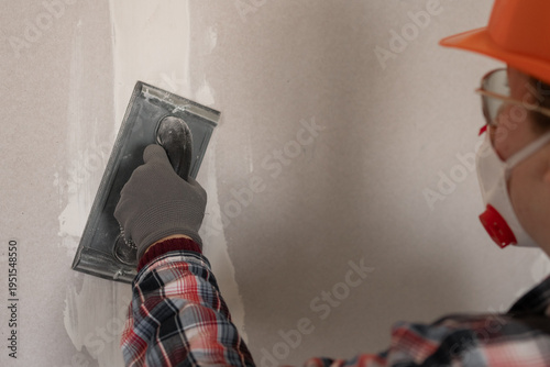 Fotografie Woman builder repairman with an emery tool sanding a plastered wall