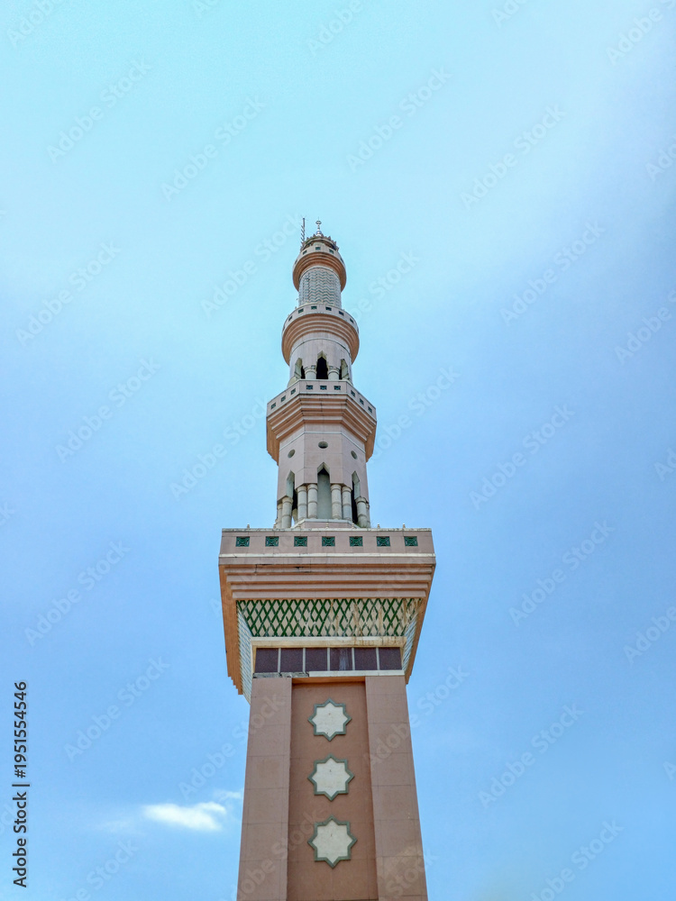 Fototapeta premium Low angle view of a tall mosque minaret under a clear blue sky. Islamic architecture, religious landmark, and traditional tower design with star ornaments.